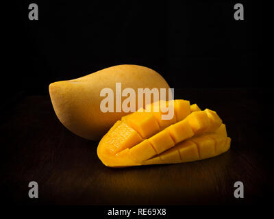 Side view image of close up appetizing yellow mango fruit and mango cubes on wooden table on black backbround Stock Photo