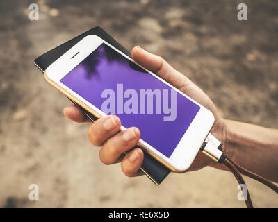 Human hands holding white smartphone charging battery from external power bank in outdoor Stock Photo