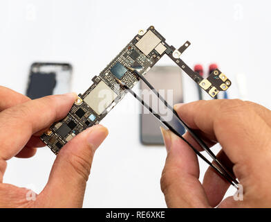 Close-up of technician hand clamping processor on smartphone logic board on blurred smartphone component background Stock Photo