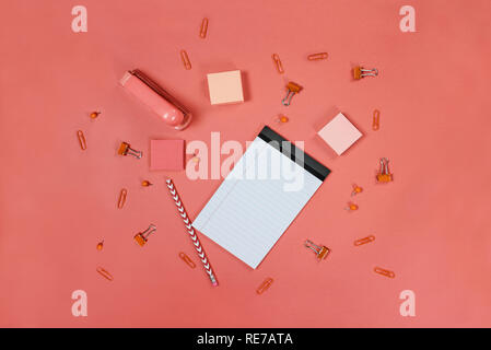 Blank white note pad paper, pencil, stapler, thumb tacks, paper clips, and adhesive paper over coral color background with free space for text. Image  Stock Photo