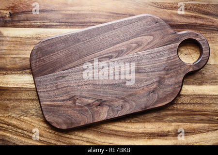 Walnut wooden cutting board with round handle hold over oak table top. Image shot from above in flat lay position. Stock Photo