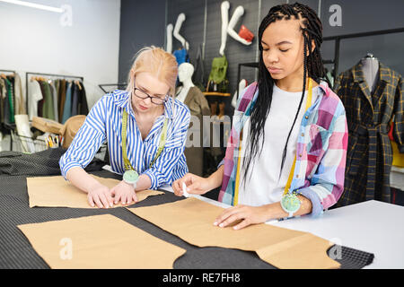 Two young fashion designers drawing sketches on fabric together at tailors table in workshop Stock Photo