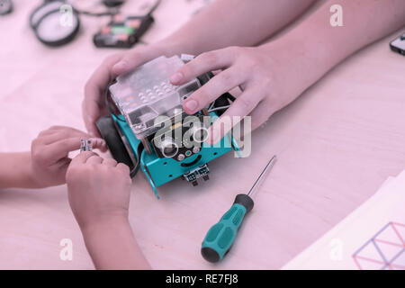 Hands of children gathering a model of controlled all-terrain vehicle, home-made robotic toy. Concept of children's hobby, learning, technology, learning, engineering Stock Photo