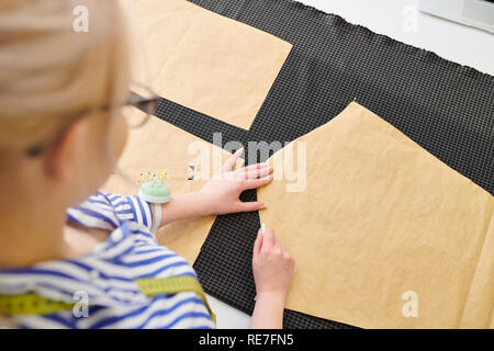 Young fashion designer making white chalk markings of paper patterns on fabric before cutting details for future jacket or costume Stock Photo