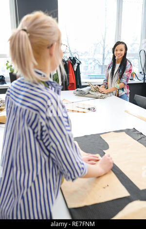 Young female designer choosing fabric and talking to dressmaker in atelier Stock Photo