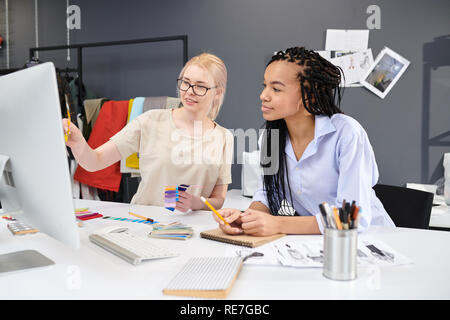 Two fashion designers working in team at the table, they using colorful palette and looking at computer monitor Stock Photo
