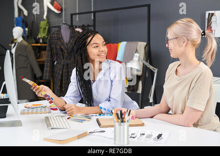 Two female designers sitting at office table working with colorful palette and computer and discussing their future plans Stock Photo