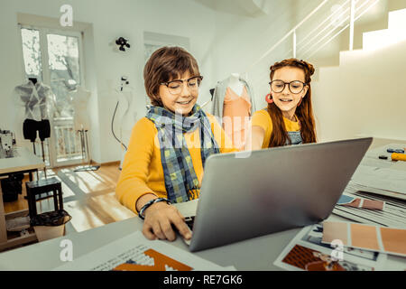 Dark-haired boy wearing yellow sweater and blue scarf using laptop Stock Photo