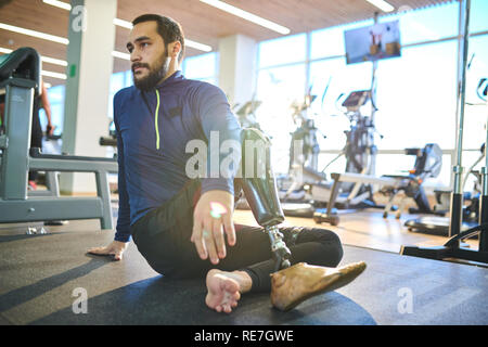 Bearded athlete with amputee leg sitting on the floor and resting in health club Stock Photo