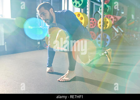Tired handsome young bearded man with prosthetic leg standing on one knee and leaning on hand while resting after exercise in gym, lens flare effect Stock Photo