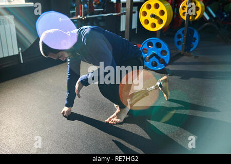 Serious exhausted handicapped young man with prosthetic leg leaning on hand while sitting on one knee, he resting after training in gym Stock Photo