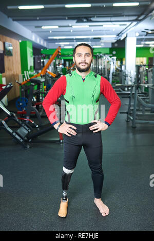 Content confident handsome handicapped young man in sports clothing standing in modern gym and looking at camera while holding hands on hips Stock Photo