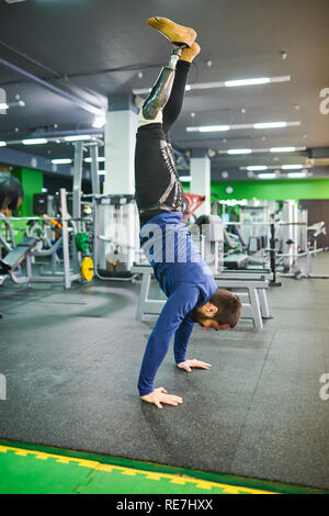 Strong skilled young bearded man  with prosthetic leg keeping balance while standing on hands in modern gym Stock Photo