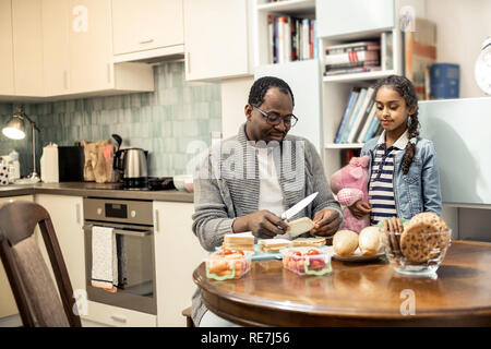 Cute daughter with pink toy watching father cooking breakfast Stock Photo
