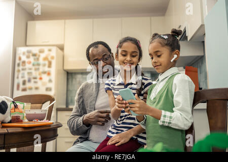 Cute modern daughters using their smartphone standing near father Stock Photo