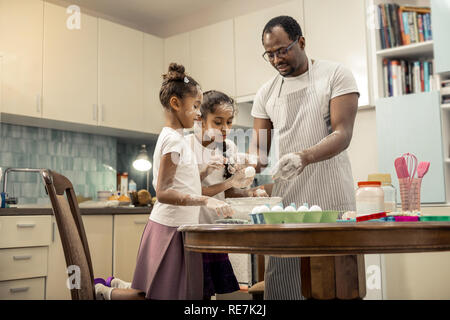Father and daughters standing near table in kitchen cooking together Stock Photo