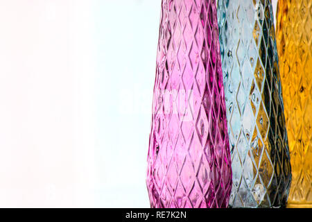 Three vases of colored glass with a pattern, close-up, isolated on a light background. Stock Photo