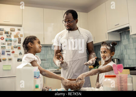 African-American man in apron cooking chocolate pie with daughters Stock Photo