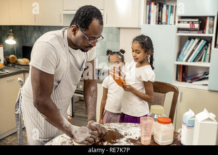 Cute daughters coming to their father cooking in the kitchen Stock Photo