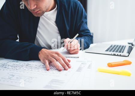 Close-up of hands architect uses laptop and building blueprint on working table in office space. Young engineer working on building plan Stock Photo