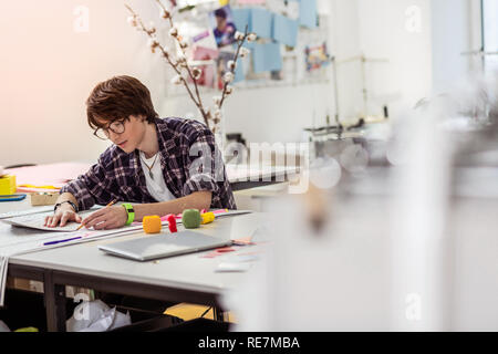 Young dark-haired asian designer with a green watch looking concentrated Stock Photo