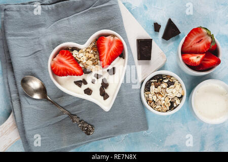 Yogurt with muesli and strawberries in a heart-shaped bowl on a pastel blue background.Yogurt with muesli and strawberries in a heart-shaped bowl on a Stock Photo