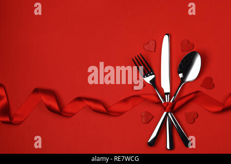 Cutlery set tied with silk ribbon and hearts on red background Valentine day dinner concept Stock Photo