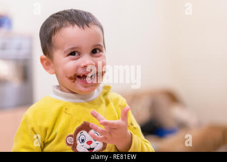 Happy child licks a spoon with chocolate. Happy boy eating chocolate cake. Funny baby eating chocolate with a spoon. dirty happy child Stock Photo