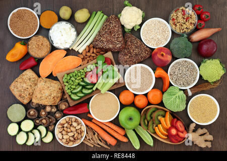 Health food for vegans with grains, seeds, nuts, peanut butter, almond yoghurt, herbs, spice, vegetables, fruit, cereals, wholegrain bread rolls. Stock Photo