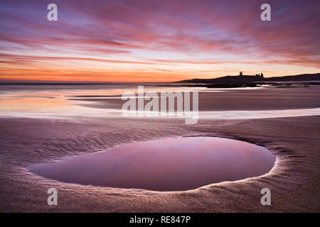 Dunstanburgh Castle at sunrise across Embleton Bay, Northumberland, England Stock Photo