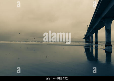 New Brighton Pier, long pier disappearing into sea at low tide on wet calm day. Christchurch New Zealand Stock Photo