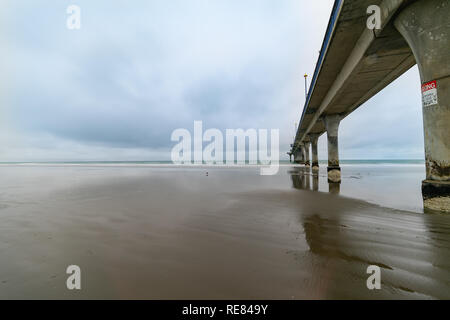 New Brighton Pier, long pier disappearing into sea at low tide on wet calm day. Christchurch New Zealand Stock Photo