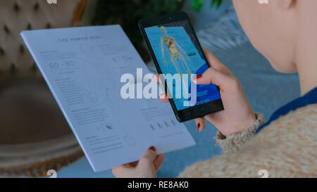 MOSCOW, RUSSIA - AUGUST 10, 2018. Woman using smartphone with augmented reality app - educational anatomy human body system. Future, medical and technology concept Stock Photo
