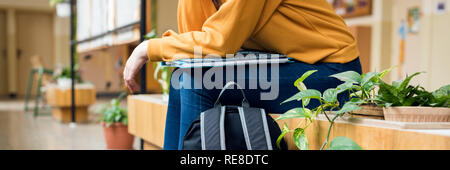 Young unrecognisable depressed lonely female college student sitting in the hallway at her school. Education, Bullying, Depression concept. Stock Photo