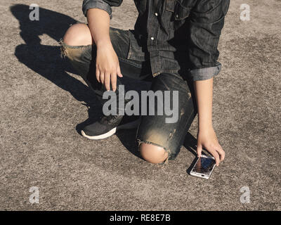 Young man picking broken and cracked screen smartphon from floor after dropped. Concept of broken or accident mobile phone, repair, warranty and techn Stock Photo