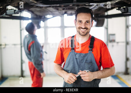 Two mechanics in uniform are working in auto service with lifted vehicle Stock Photo