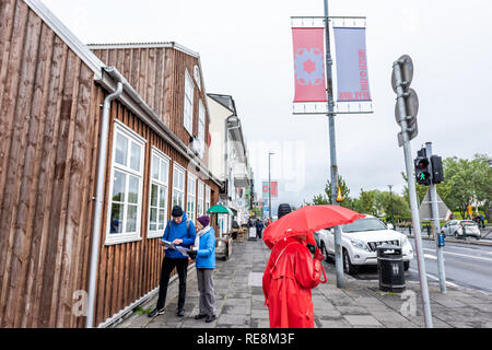 Reykjavik, Iceland - June 19, 2018: People tourists walking on street with red umbrella checking map directions on sidewalk in downtown center Stock Photo