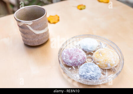 Green tea ceramic cup and mochi rice cake Japanese dessert wagashi colorful daifuku pieces on autumn season leaves on table color Stock Photo