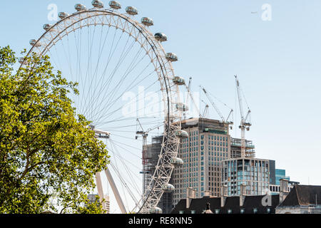 London, UK - June 22, 2018: Cityscape skyline view of London Eye capsules in city and blue sky ferris wheel and construction cranes during sunny day w Stock Photo