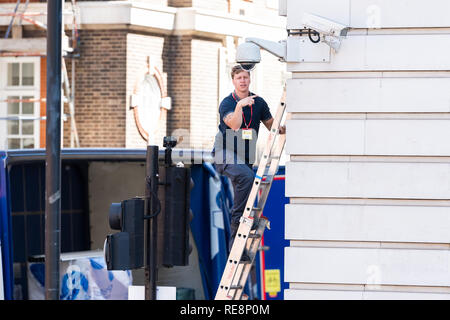 London, UK - June 22, 2018: Employee contractor worker climbing ladder on street building to replace security camera near Whitehall Stock Photo