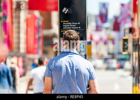 London, UK - June 22, 2018: Back of one man standing reading looking at map for directions to SoHo on Piccadilly sidewalk street road in downtown city Stock Photo
