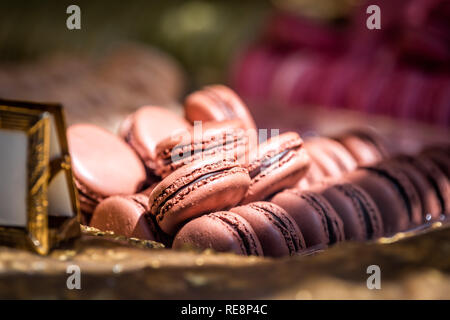 Display of pile of gourmet colorful pink red velvet chocolate macaroons macarons on shelf in bakery store shop Stock Photo