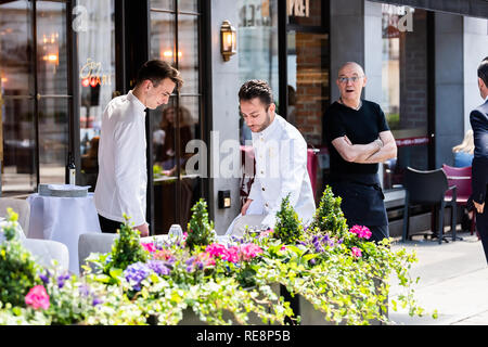 London, UK - June 22, 2018: Men waiters standing setting up cafe table in Regent street during training with manager owner outdoor outside restaurant  Stock Photo