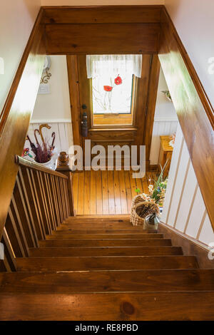 Brown stained pinewood staircase leading down to ground floor and entrance door with stained glass window inside old 1892 Canadiana cottage style home. Stock Photo