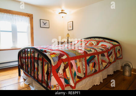 Double bed with bright multicoloured patterned bedspread and wrought iron headboard and footboard in upstairs guest bedroom, inside an old 1892 house Stock Photo