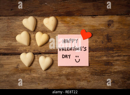 Beautiful top view Valentines composition of heart shaped chocolates and Happy Valentines day note written on post it in vintage style wooden table ba Stock Photo