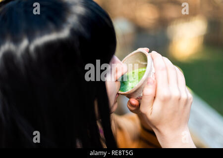 Woman holding tea cup face closeup drinking outside in backyard garden with girl and green matcha black hair Stock Photo