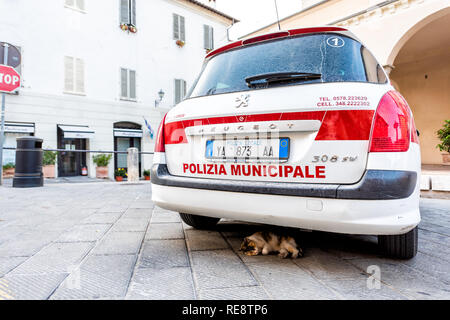 Chiusi, Italy - August 25, 2018: Empty street in small town village in Umbria during day with Italian police car and sign with stray cat sleeping unde Stock Photo