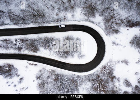 Aerial view of a beautiful serpentine road with some cars that run through it. Spectacular landscape consisting of a pine trees forest and white snow. Stock Photo