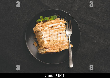 Russian honey cake Medovik on black plate, top view, toned image Stock Photo